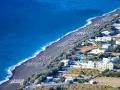 Santorini plaże z czarnym piaskiem, rzędy leżaków i białe budynki hotelowe nad turkusowym morzem.
