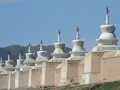 Białe stupy wzdłuż muru w Karakorum, na tle łagodnych wzgórz i błękitnego nieba.