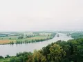 Szeroka rzeka na tle zielonych pól i lasów. W oddali widać most i zabudowania.