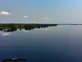 Szeroka, spokojna rzeka Kongo, odbijająca niebo i bujną zieleń brzegów. Na wodzie płynie łódź z kilkoma osobami.