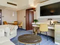 Elegancki pokój w hotelu Diament Wrocław: biała sofa, złote krzesła, biurko z telefonem i kwiatami, stolik kawowy.