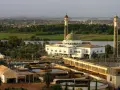 Meczet z zieloną kopułą i dwoma minaretami nad rzeką, z widokiem na miasto i zakłady przemysłowe.
