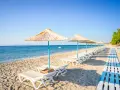 Plaża na wyspie Kos. Rzędy leżaków pod słomianymi parasolami, drewniana ścieżka i spokojne morze.