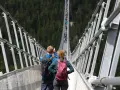 Para idzie przez wiszący most w Czechach, podziwiając widok na las.