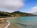 Piękna plaża Tragaki Zakynthos z turkusową wodą, zielonymi wzgórzami i rzędem leżaków pod parasolami.