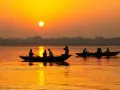 Łodzie na rzece Ganges podczas zachodu słońca. Ludzie płyną łodziami po wodzie, odbijając się w pomarańczowym blasku.