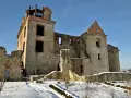Kamienne ruiny dawnego monastyru w zimowej scenerii. Widać zniszczone mury, łuki okienne i wieżę z platformą widokową.