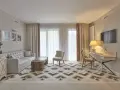 Elegancki pokój w hotelu 5 gwiazdkowym: sofa, stolik, fotele, biurko i TV. Wzory na dywanie i zasłonach dodają charakteru.