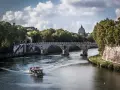 Łódź płynie po Tybrze w kierunku mostu, za którym widać kopułę Bazyliki św. Piotra. Stolica nad Tybrem w pełnej krasie.