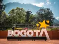 Napis BOGOTA z żółtymi gwiazdami, symbolizujący stolicę Kolumbii, na tle zielonych wzgórz i błękitnego nieba.