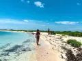 Kobieta spaceruje po piaszczystej plaży nad turkusową wodą. W tle widać innych ludzi i bujną zieleń. To idealne miejsce na wypoczynek nad Zatoką Meksykańską.