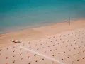 Pusta plaża w Rimini z rzędem pomarańczowych parasoli i turkusową wodą. Na piasku stoi mała łódź.