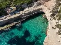 Malta plaże: turkusowa woda w zatoce, skaliste wybrzeże i mały domek. Dwie osoby spacerują ścieżką.