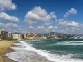 Malaga plaże z falami rozbijającymi się o brzeg i miastem w tle.