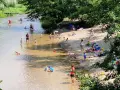 Słoneczny dzień nad Świdrem. Ludzie odpoczywają na piaszczystej plaży i kąpią się w rzece. Dzieci bawią się w wodzie.