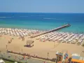 Słoneczny Brzeg, Bułgaria: tłumy plażowiczów, białe parasole, molo i turkusowe morze.