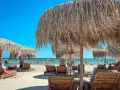 Słoneczne rumuńskie wakacje nad morzem. Leżaki i parasole z trawy na piaszczystej plaży, w tle ludzie kąpiący się w morzu.