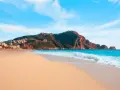 Plaża Kleopatry w Alanyi, z turkusowym morzem, piaszczystym brzegiem i górującym nad nią skalistym masywem z twierdzą.
