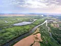 Malownicza dolina rzeki Odry z licznymi meandrami, zielonymi łąkami, polami i niewielką wsią po prawej stronie.