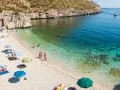 Sycylia plaże: kamienista zatoczka z turkusową wodą, ludzie odpoczywają pod parasolami, pływają i opalają się.