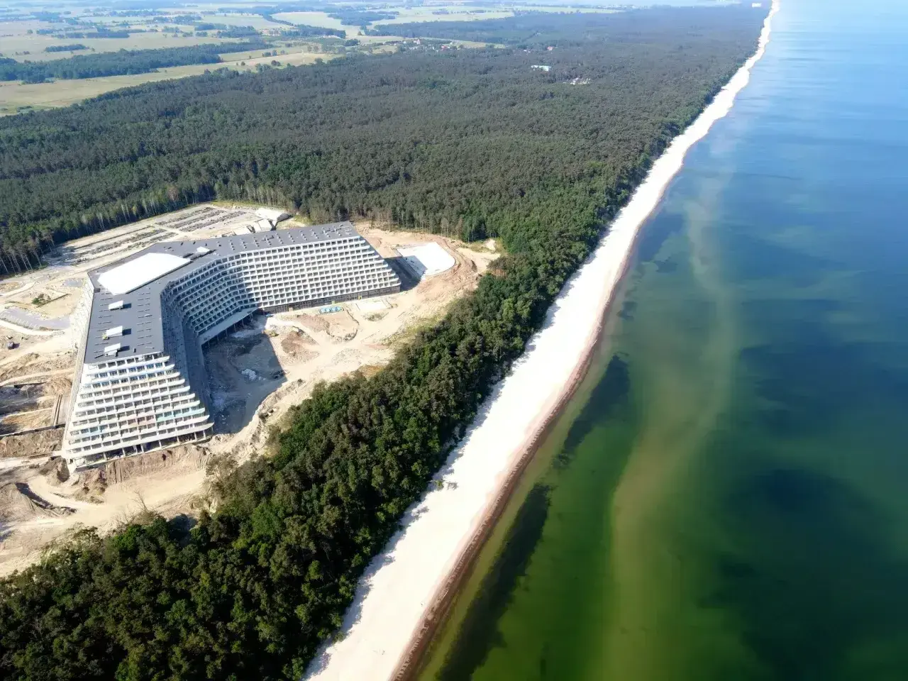 Nowy hotel Gołębiewski nad morzem, w otoczeniu lasu sosnowego i szerokiej plaży, z widokiem na turkusowe wody Bałtyku.
