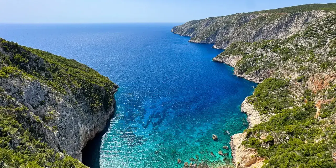 Widok na zatokę z klifami porośniętymi zielenią. Idealne miejsce na zakynthos wycieczki fakultatywne, by podziwiać turkusową wodę.