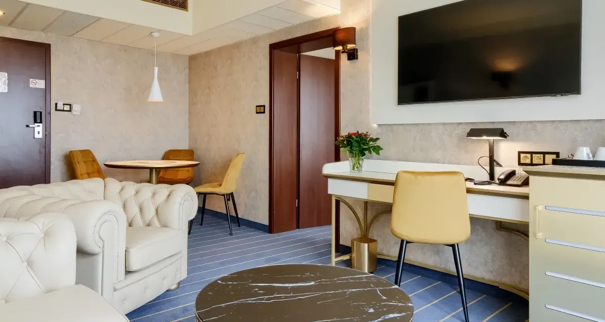 Elegancki pokój w hotelu Diament Wrocław: biała sofa, złote krzesła, biurko z telefonem i kwiatami, stolik kawowy.