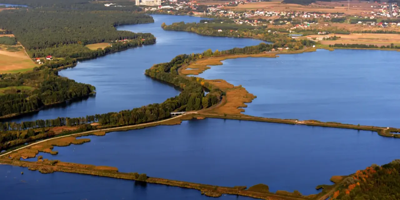 Widok z lotu ptaka na jezioro z wyspami, lasami i zabudowaniami w tle.