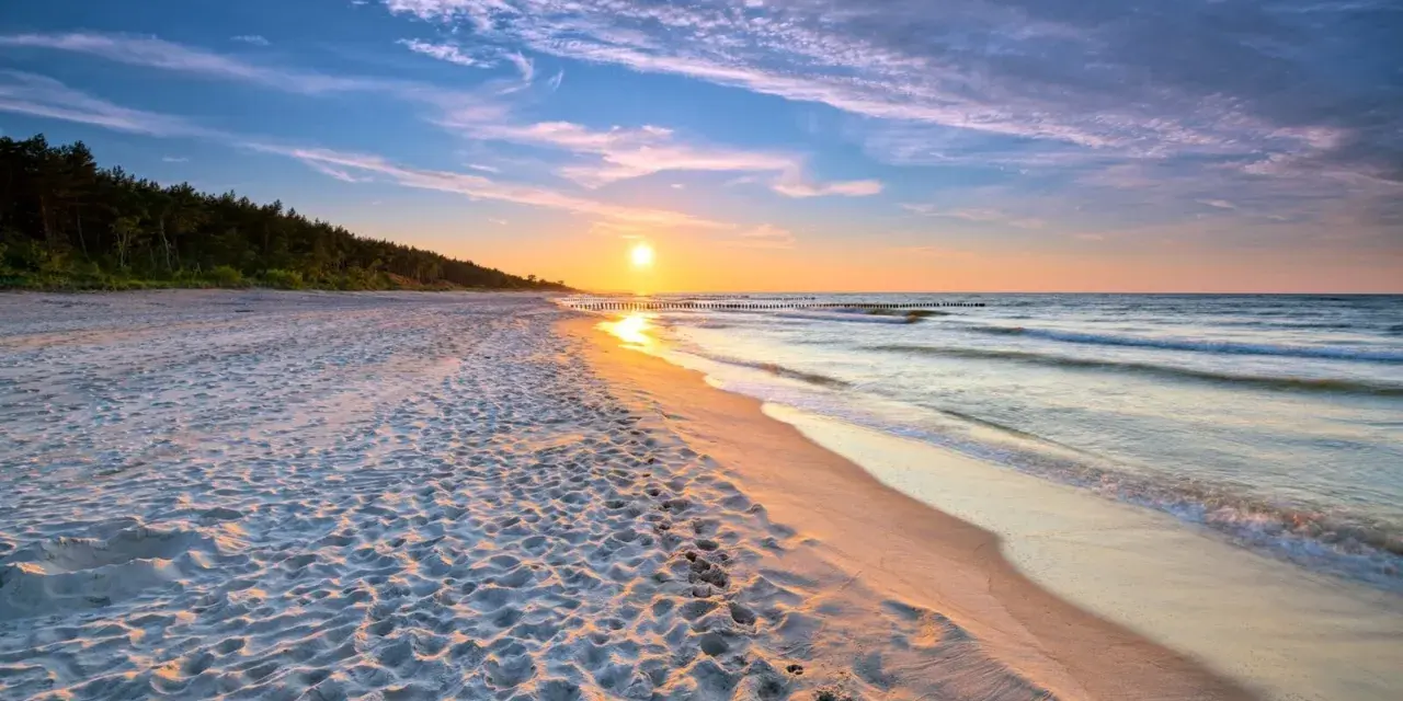 Zachód słońca nad morzem, piaszczysta plaża z odciskami stóp, las w tle. Idealne, fajne miejsce nad morzem dla dwojga na romantyczny spacer.