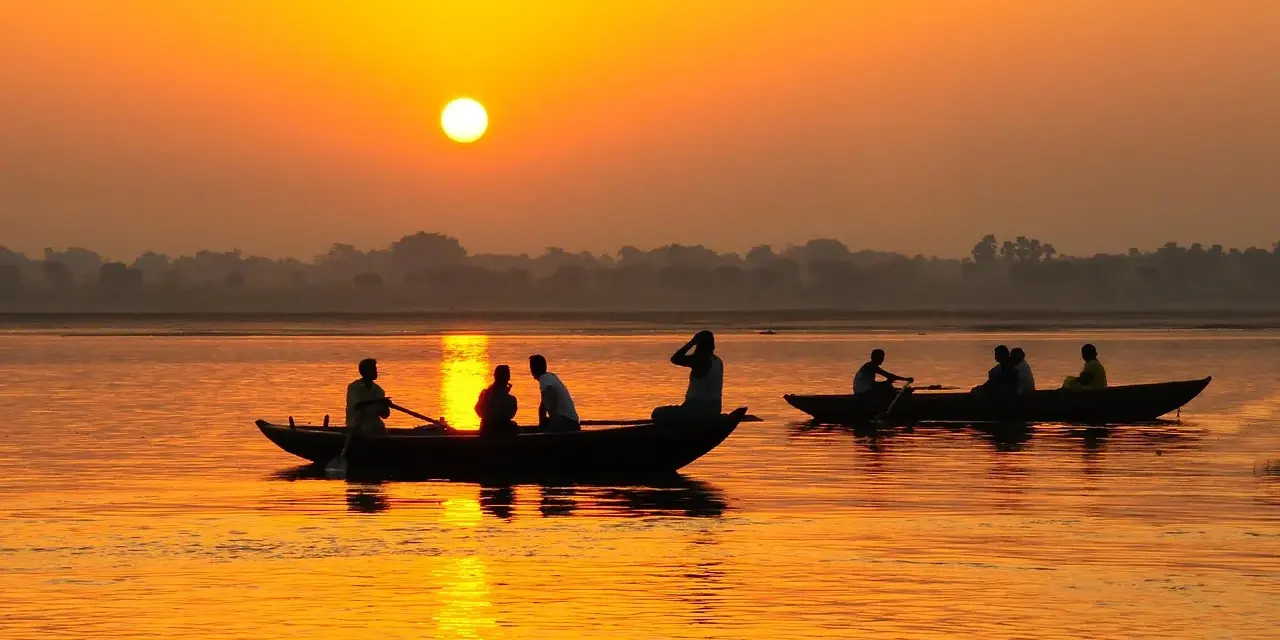 Łodzie na rzece Ganges podczas zachodu słońca. Ludzie płyną łodziami po wodzie, odbijając się w pomarańczowym blasku.