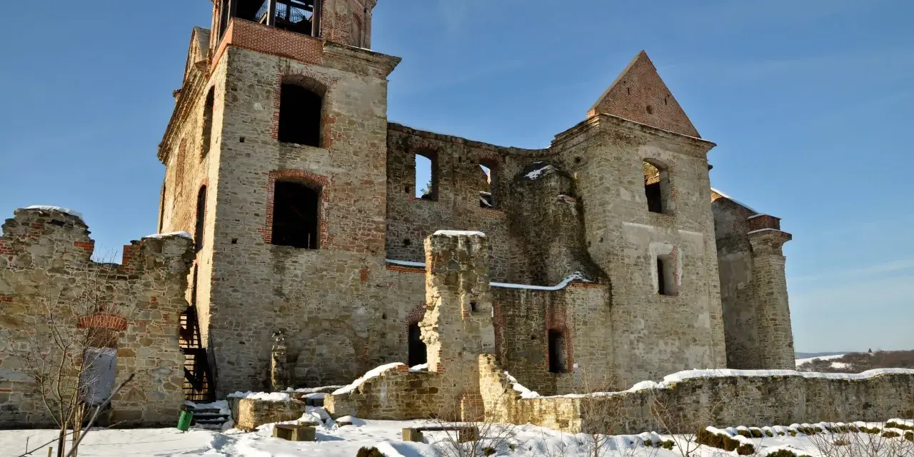 Kamienne ruiny dawnego monastyru w zimowej scenerii. Widać zniszczone mury, łuki okienne i wieżę z platformą widokową.