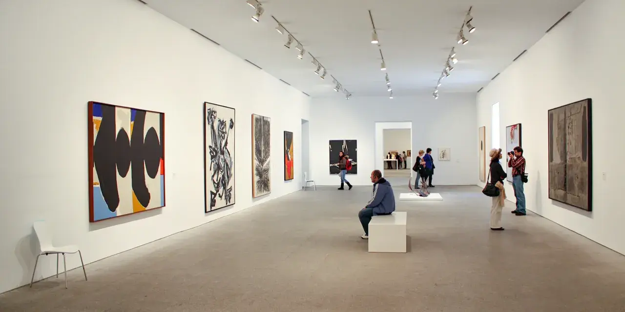Wnętrze muzeum w Madrycie. Zwiedzający podziwiają abstrakcyjne obrazy i rzeźby, niektórzy robią zdjęcia.