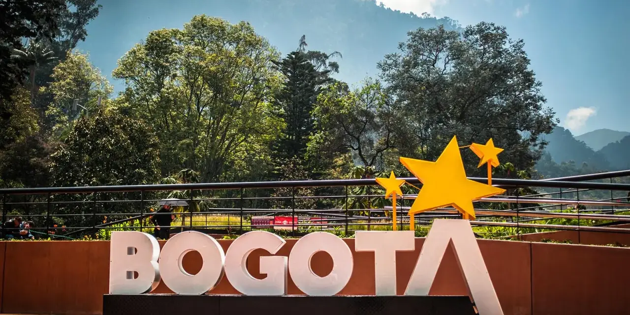 Napis BOGOTA z żółtymi gwiazdami, symbolizujący stolicę Kolumbii, na tle zielonych wzgórz i błękitnego nieba.