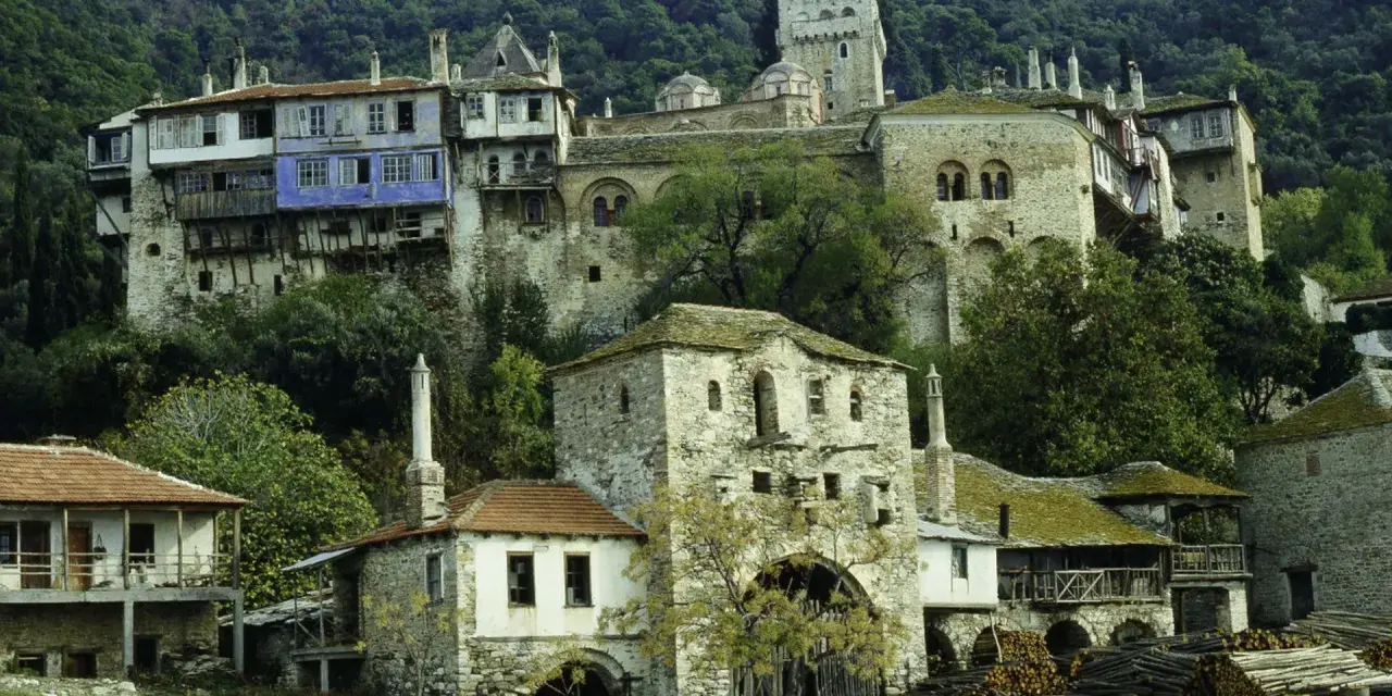 Kamienne budynki klasztorne na zboczu góry Athos, z niebieskim akcentem na jednym z nich.