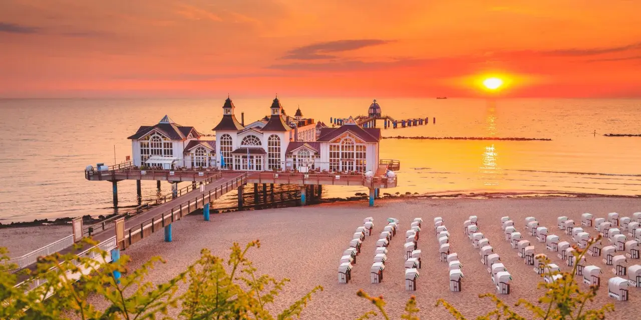 Zachód słońca nad molo w Sellin, na Rugii, największej wyspie Niemiec. Puste kosze plażowe czekają na gości.