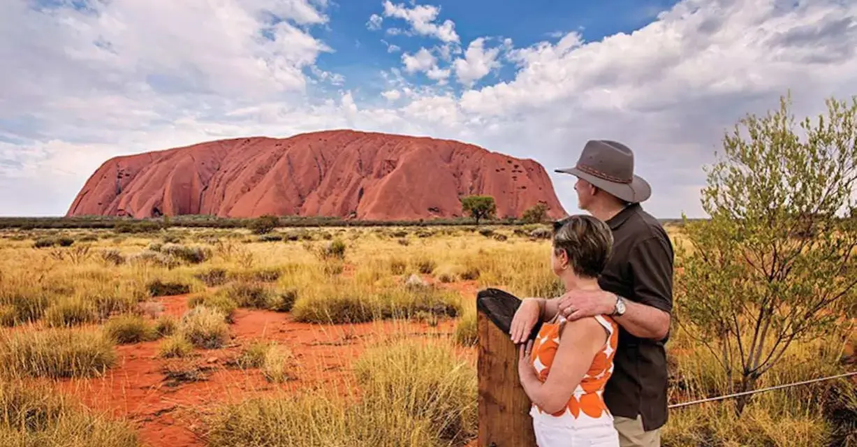 Para turystów podziwia Uluru, świętą skałę rdzennych mieszkańców Australii, w pustynnym krajobrazie.