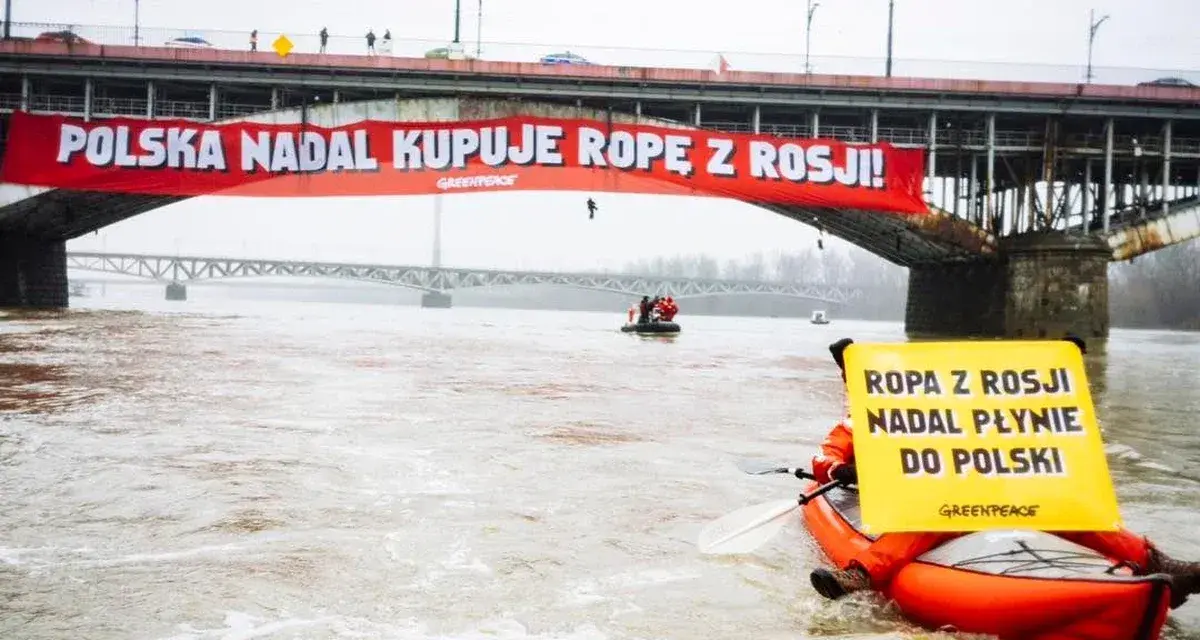 Na moście Poniatowskiego wisi czerwony baner "Polska nadal kupuje ropę z Rosji!". Kajakarz Greenpeace na Wiśle trzyma żółtą tablicę "Ropa z Rosji nadal płynie do Polski".