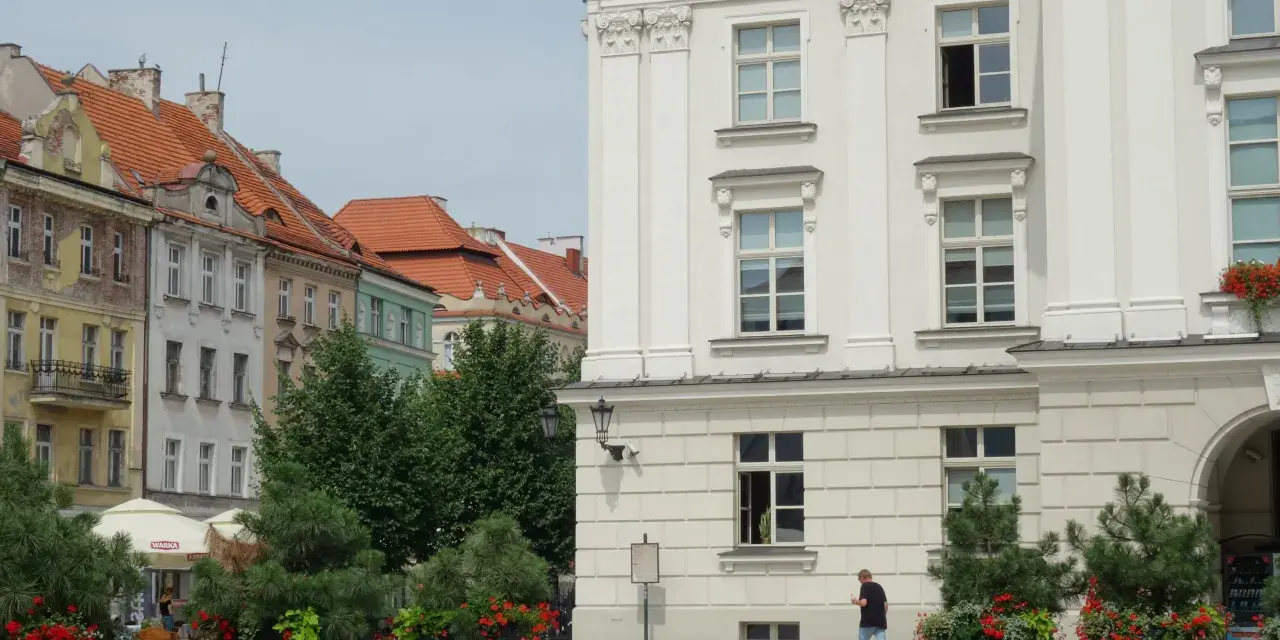 Urokliwe miasto nad Prosną z zabytkową architekturą, zielenią i ławkami w centrum.