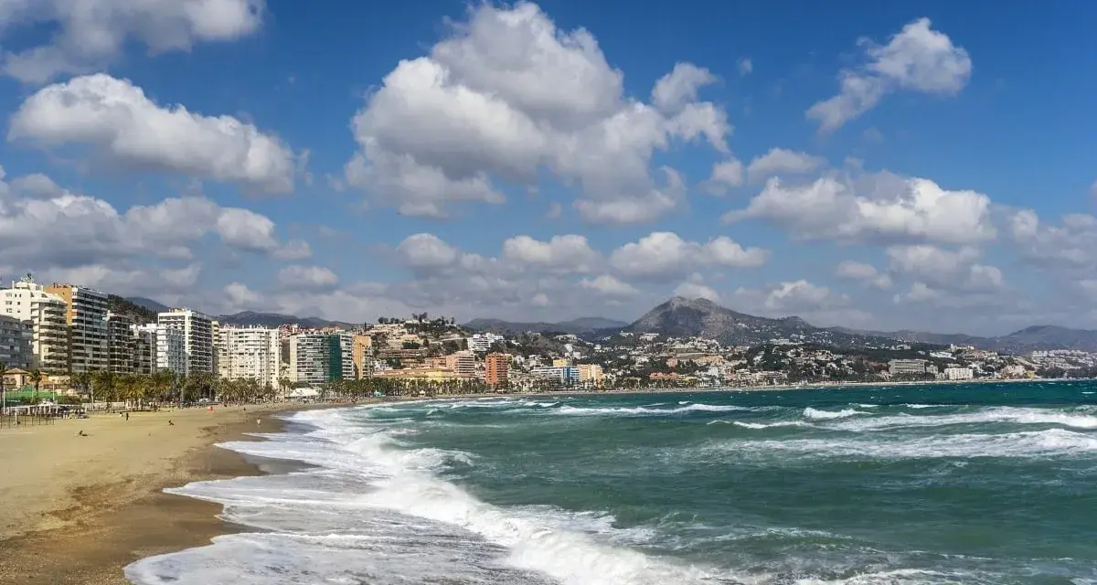 Malaga plaże z falami rozbijającymi się o brzeg i miastem w tle.