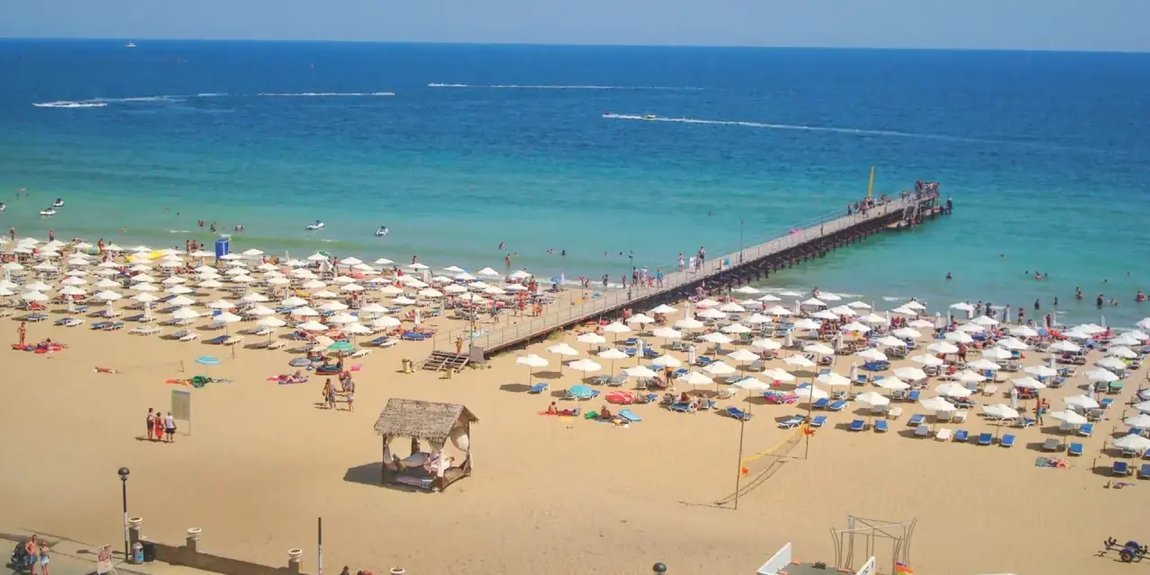 Słoneczny Brzeg, Bułgaria: tłumy plażowiczów, białe parasole, molo i turkusowe morze.