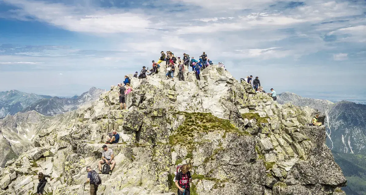 Tłum turystów na skalistym szczycie Rysów, najwyższego szczytu w Polsce, podziwia rozległą panoramę Tatr.