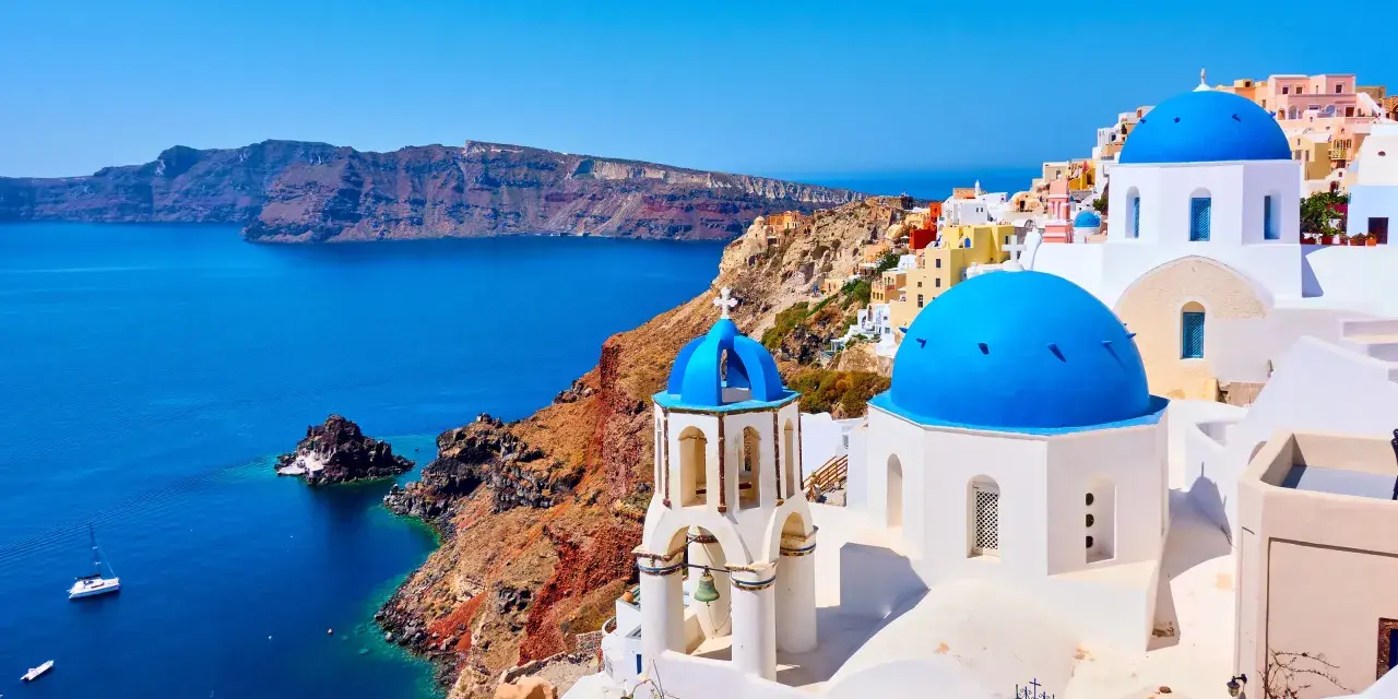 Santorini wakacje: białe domy z niebieskimi kopułami na tle turkusowego morza i klifów. Idealne miejsce na wymarzone wakacje.