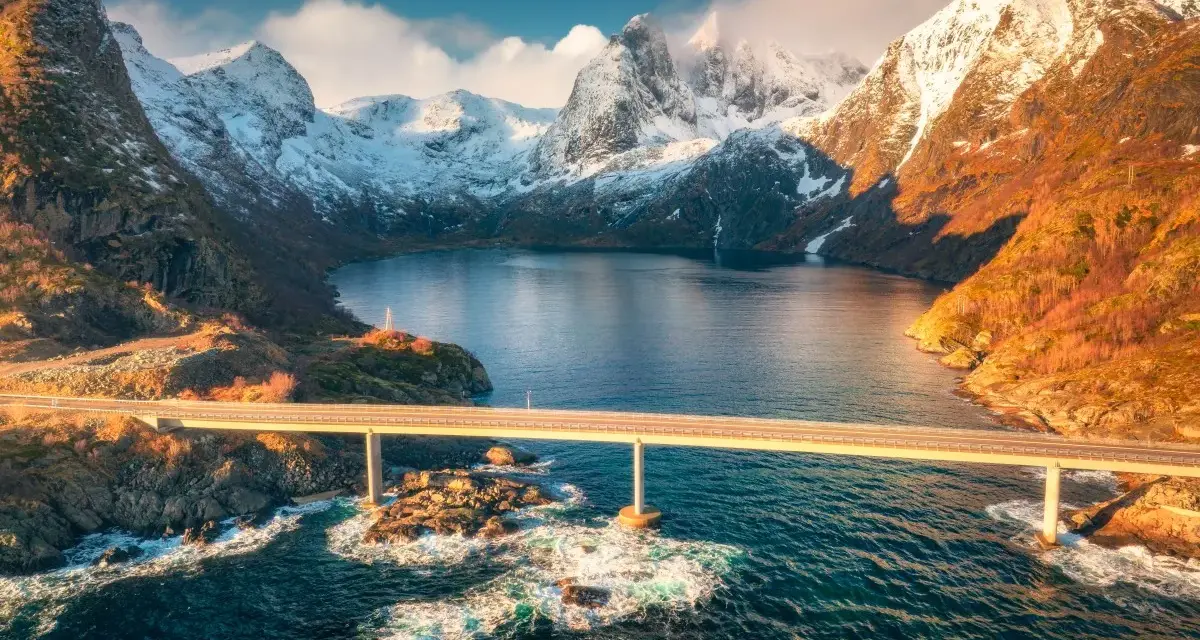Mosty łączące wyspy w fiordach Norwegii, z ośnieżonymi górami w tle.