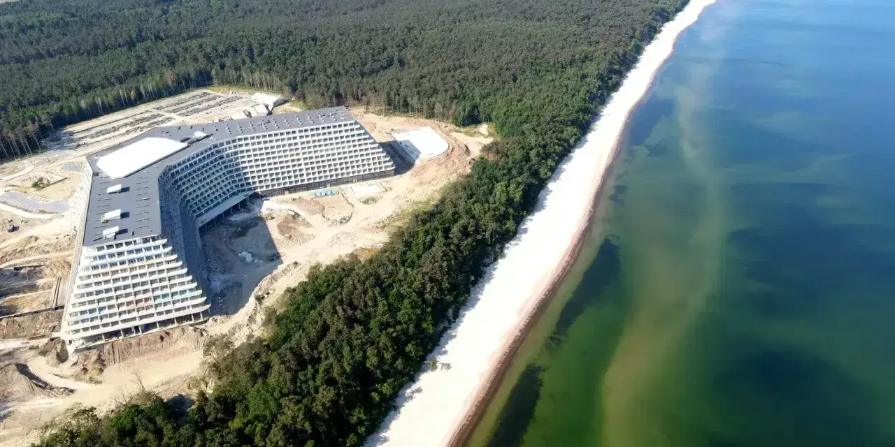 Nowy hotel Gołębiewski nad morzem, w otoczeniu lasu sosnowego i szerokiej plaży, z widokiem na turkusowe wody Bałtyku.