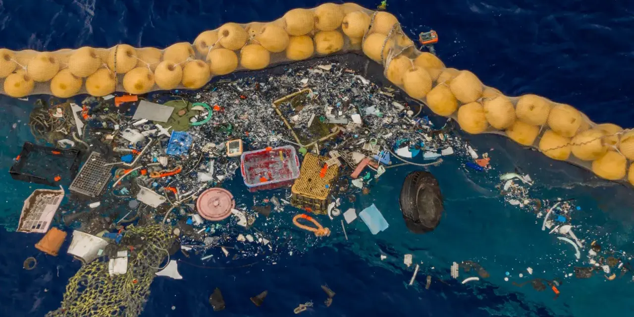 Ogromna wyspa śmieci na oceanie, zebrana w siatkę z bojami. Plastikowe odpady, sieci rybackie i opona tworzą przygnębiający widok.