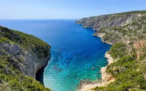 Widok na zatokę z klifami porośniętymi zielenią. Idealne miejsce na zakynthos wycieczki fakultatywne, by podziwiać turkusową wodę.