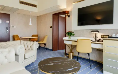 Elegancki pokój w hotelu Diament Wrocław: biała sofa, złote krzesła, biurko z telefonem i kwiatami, stolik kawowy.