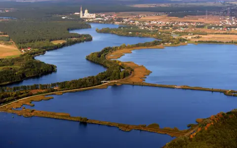 Widok z lotu ptaka na jezioro z wyspami, lasami i zabudowaniami w tle.