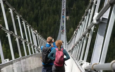 Para idzie przez wiszący most w Czechach, podziwiając widok na las.