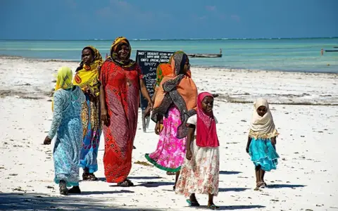 Kobiety w kolorowych strojach spacerują po plaży. Czy Zanzibar to państwo? Tak, to autonomiczny region Tanzanii, znany z pięknych plaż.